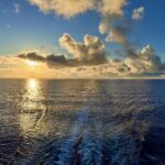 Sunset over the Atlantic Ocean viewed from a Royal Caribbean cruise ship departing Baltimore, golden light reflecting on calm waves before reaching Bermuda.