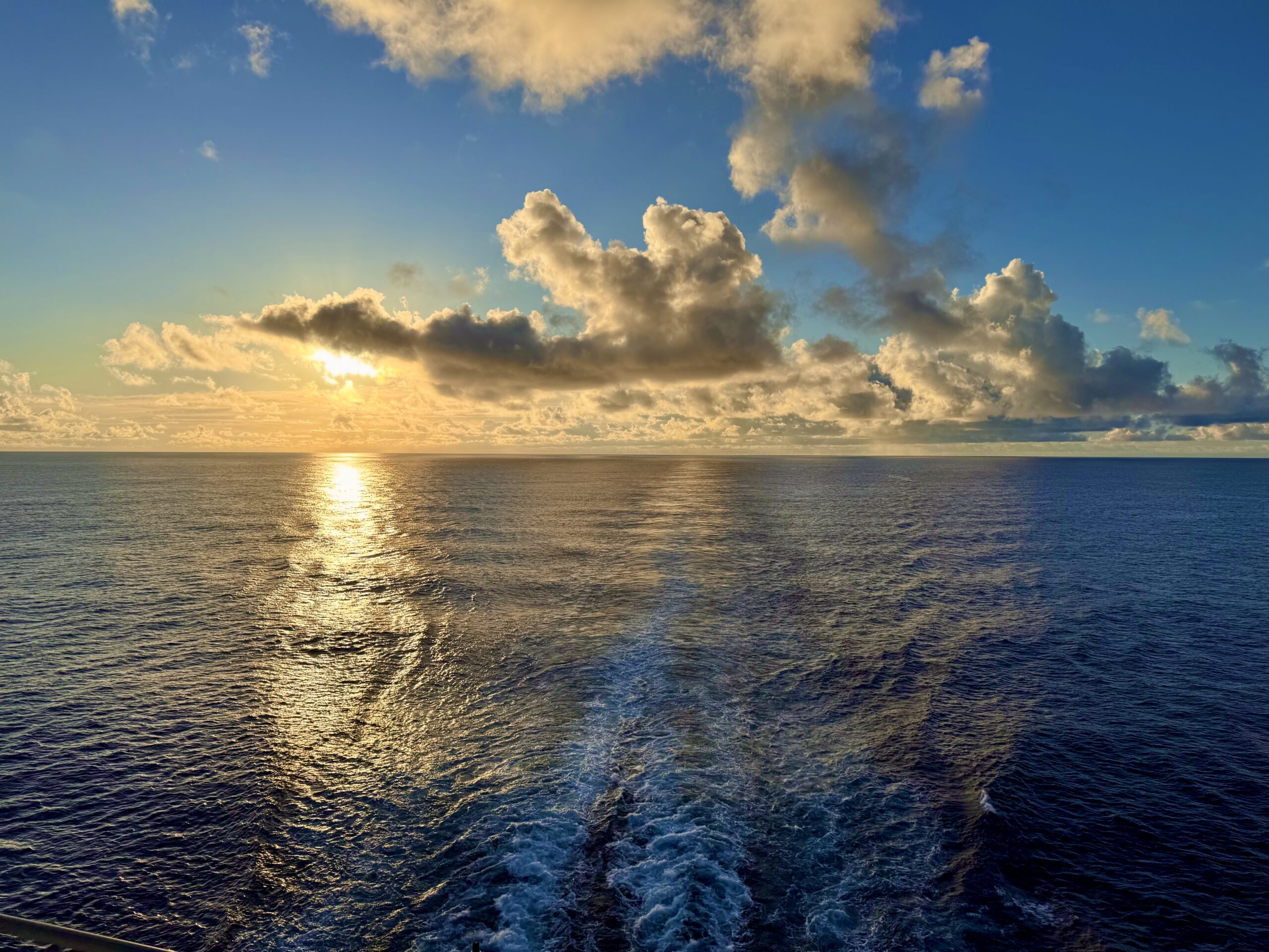 Sunset over the Atlantic Ocean viewed from a Royal Caribbean cruise ship departing Baltimore, golden light reflecting on calm waves before reaching Bermuda.