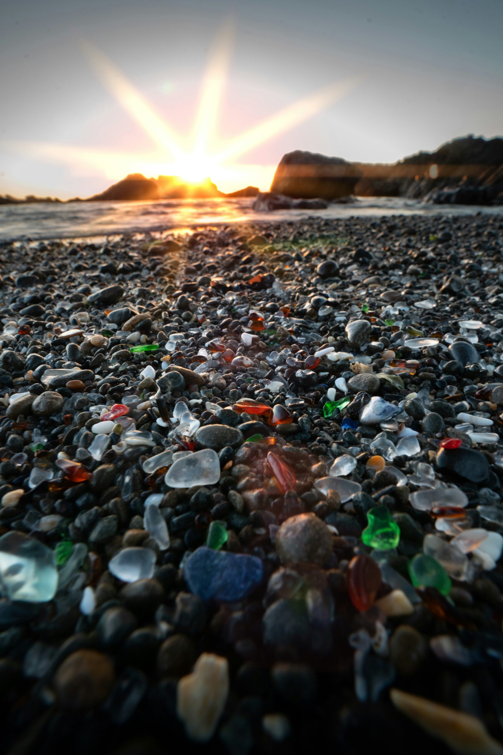 Sunrise over scattered sea glass on the beach, symbolizing transformation, patience, and growth through time.